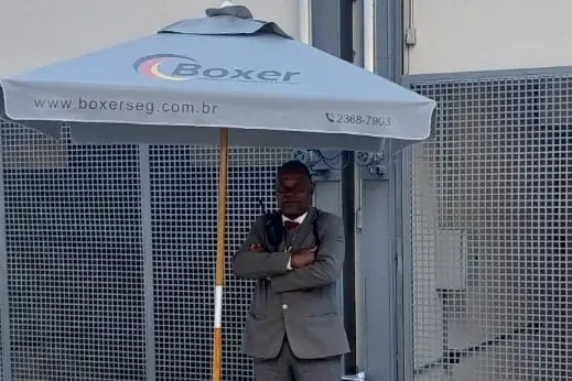 Vigilante da Boxer em posto de portaria, sob o guarda-sol da empresa